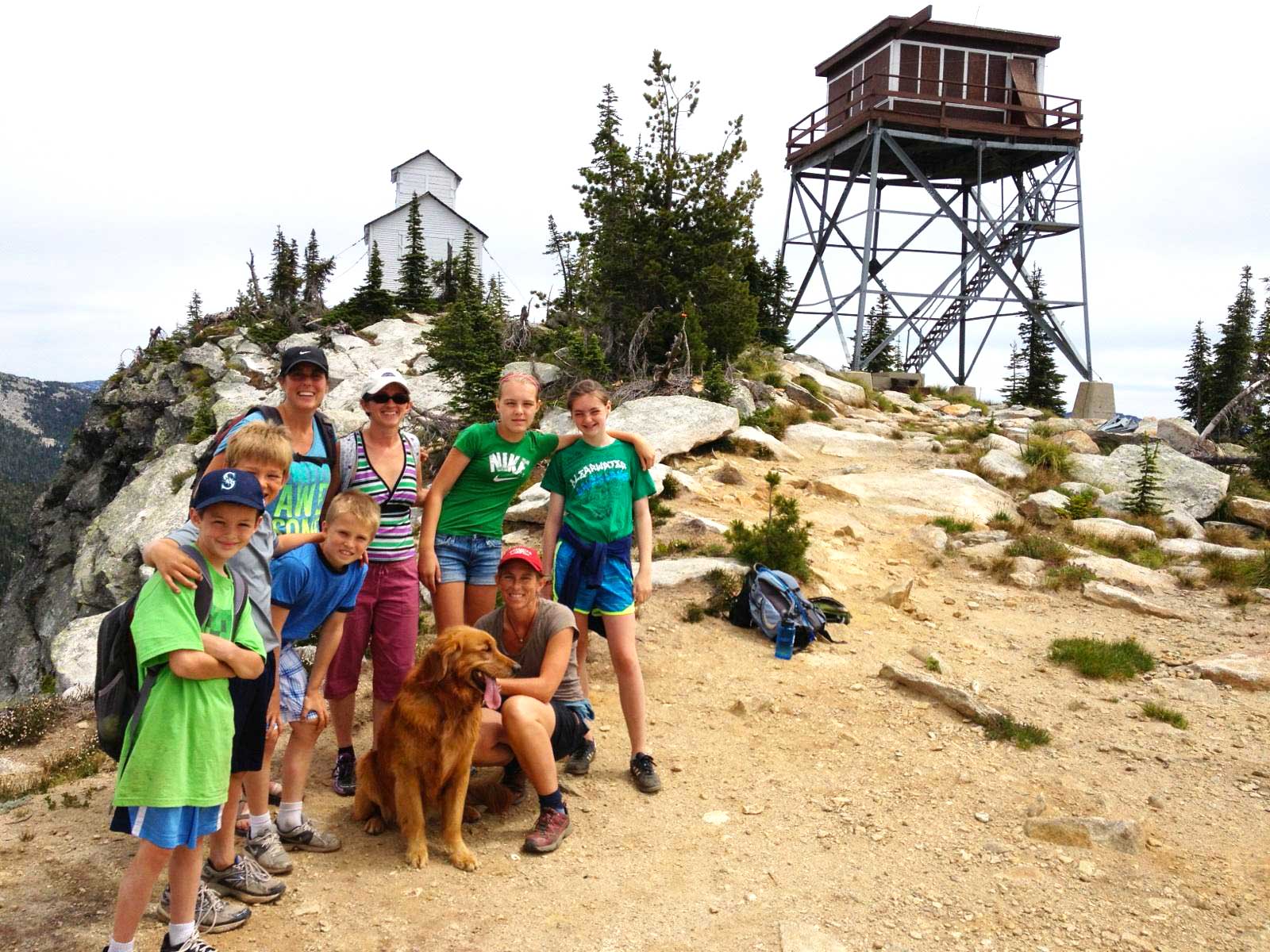 Family posing for camera at the summit of Lookout Mountain Tower, with old firelookout in the background.