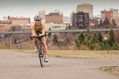 Woman cycling on the Spokane Centennial Trail with view of downtown Spokane in the background.