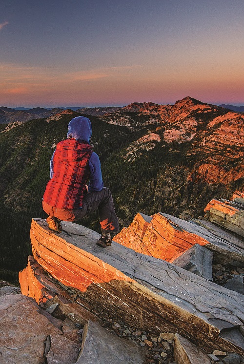 Hiker with a backpack looking at the sunset view atop rocks at Scotchman Peaks wilderness.