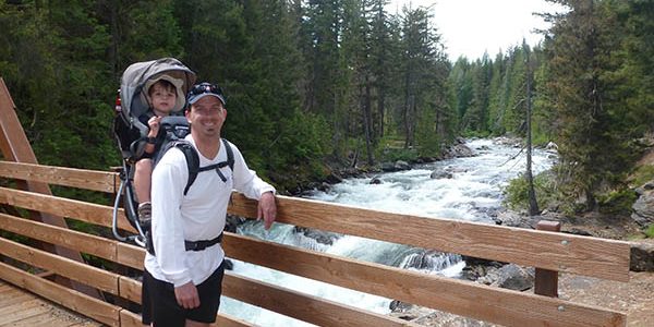 Dad with his toddler son in a backpack carrier -- standing on a bridge over the whitewater of Icicle Creek in the national forest near Leavenworth, Washington.