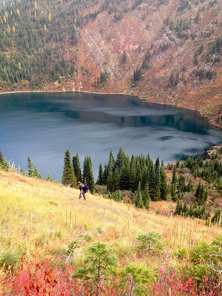 Hiker heading up a grassy slope above Lone Lake during fall.