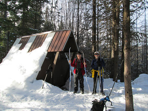 Two people snowshoeing near a hut.