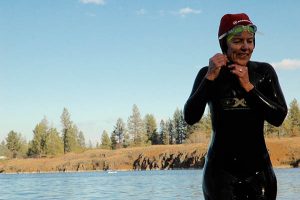 Woman in a wetsuit adjusting her swim cap, preparing for an open water swim.