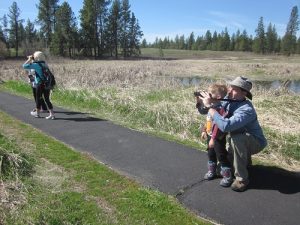 Parent and child on a trail at Turnbull National Wildlife Refuge -- looking through binoculars for birdwatching.