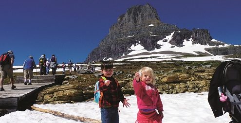 Two children holding handfuls of snow on a summertime snowfield at Logan Pass in Glacier National Park.