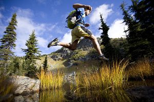 Runner jumping over a over while running in the Cabinet Mountain wilderness.