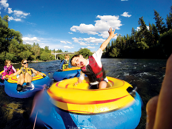 Young boy sitting in a big inflatable blue and yellow tube and floating the Spokane River during summer.