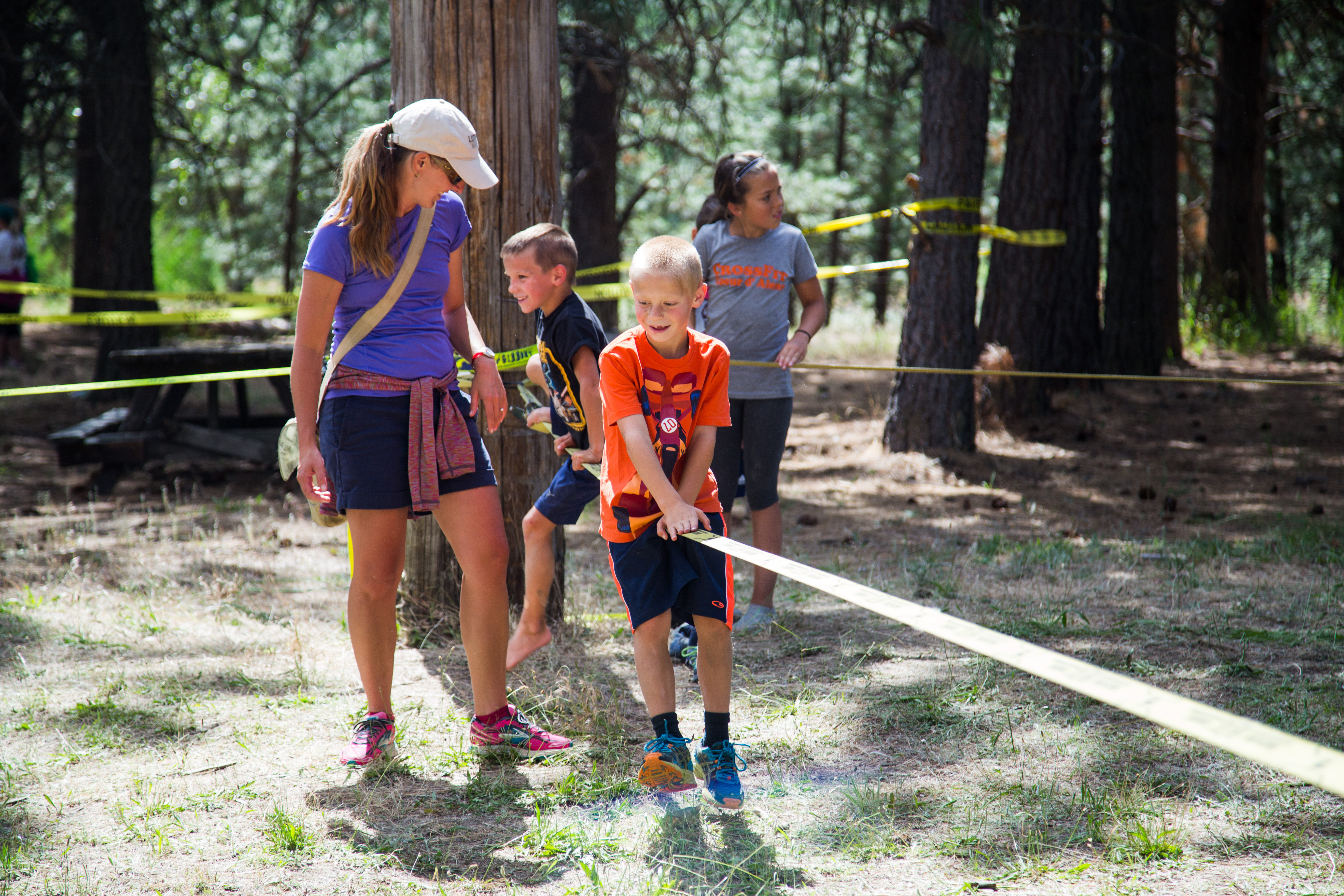 Photo of kids playing on slackline with parent watching.