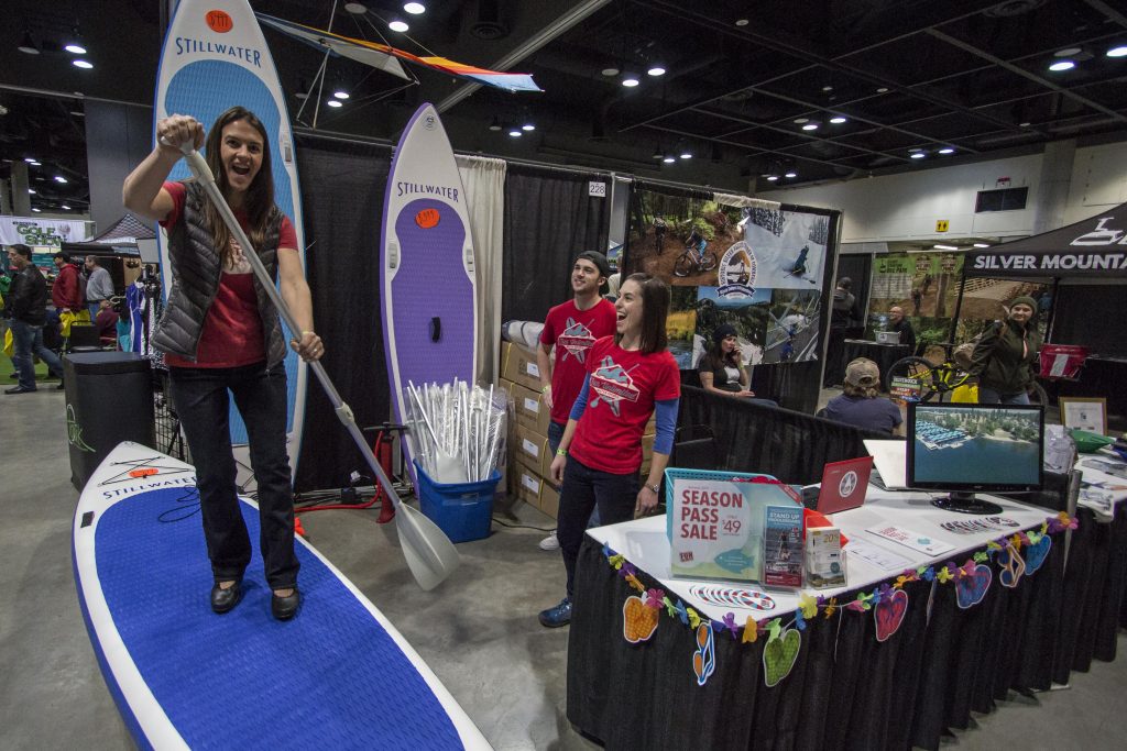 Woman standing on a paddleboard pretending to paddle indoors at the Spokane Great Outdoors & Bike Expo.