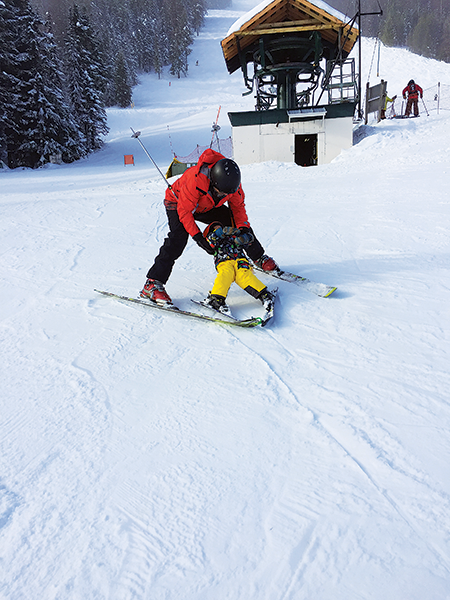 Photo of dad teaching son to ski.