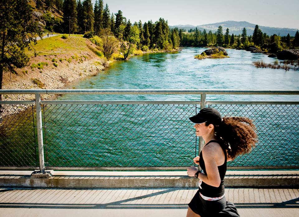 Woman running across a bridge over the Spokane River along the Windermere Marathon Centennial Trail route.