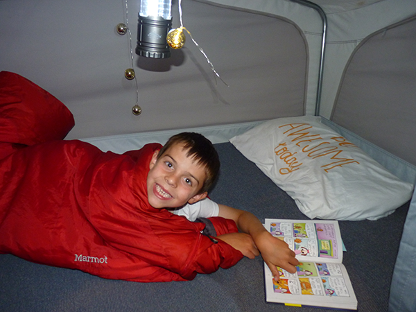 Photo of kid in sleeping bag in popup camper with a picture book.