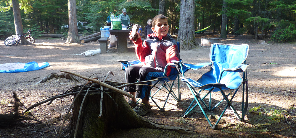 Photo of kid in front of make believe fire made from twigs and a tree stump.