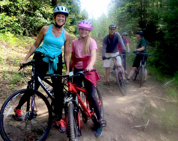 Mom, dad, and children riding mountain bikes at Spirit Lake Empire Trails. Dirt trails through evergreen forest.