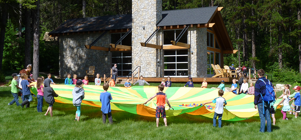 Young campers at Camp Spalding in a large circle holding onto the edge of a huge round parachute to play games.