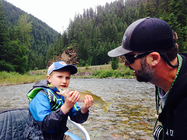 Son holding up fish with dad looking on.