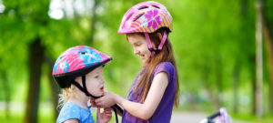 Photo of older kid buckling younger kid's helmet.
