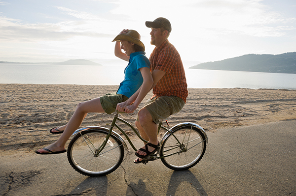 Photo of couple riding a bike along the beach.