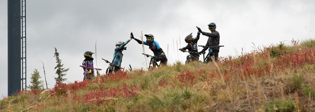 Photo of mountain bikers high-fiving underneath the gondola.