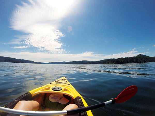 Kayak cockpit view of person sitting in a yellow kayak, with paddle across the legs, on flatwater of Lake Coeur d'Alene.om kayak.