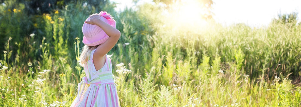 Little girl in sundress and hat in field.