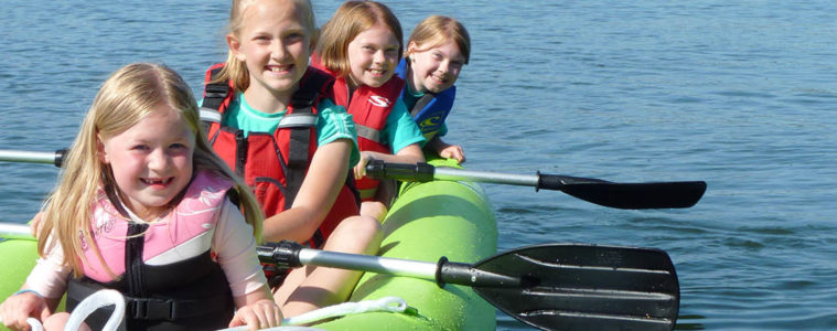 Photo of four kids in a kayak paddling on Lake Chatcolet in North Idaho.