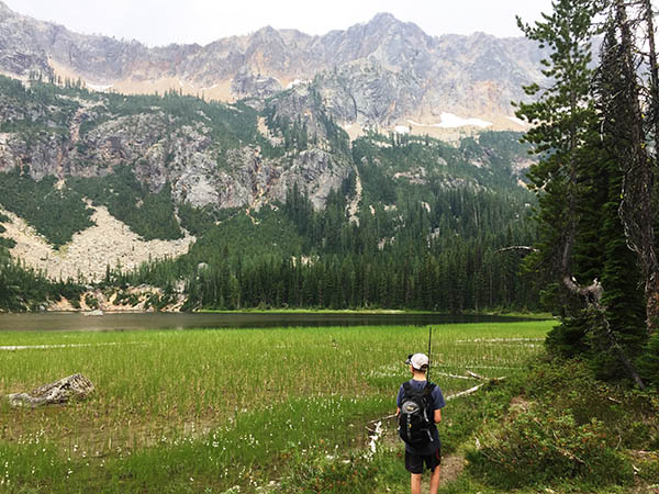 Photo of young boy hiking with alpine lake and mountains in the background.