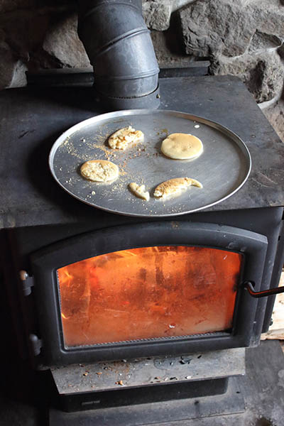 Photos of pancakes in skillet on top of wood burning stove.