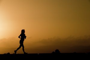 Silhouette of runner against orange sunset.