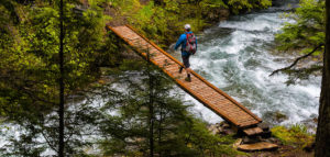 Hiker crossing wooden bridge over whitewater.