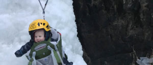 Photo of 18 month old Caleb in baby backpack hanging from a climbing anchor.