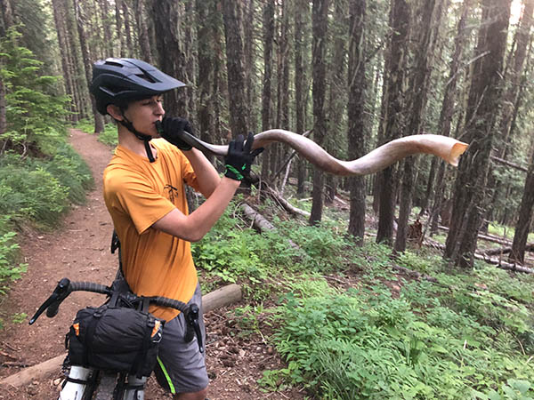 Photo of Gabe standing by his bike blowing a hunter's trumpet.