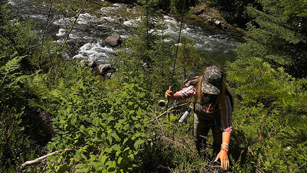 Photo of hiker scrambling up steep bank with a river in the background.