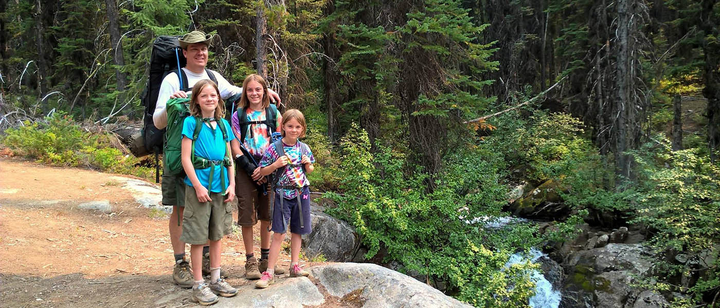 Photo of Joal Lee and his daughters posing on a rock outrcropping in Northeast Oregon's Eagle Cap Wilderness.