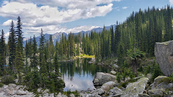 Photo of lake with trees and mountain range in distant background.