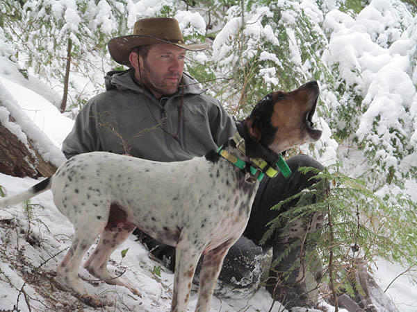 Bart reclining on a snow covered bank with a small hound dog howling in the foreground.