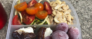 Photo of dates, nuts, grapes, and tomato pasta in a plastic lunch box.