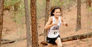 Child running on a treed dirt trail during the Camp Sekani Trail Run event.