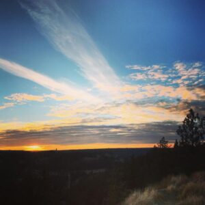 Sunset view and blue sky with streaks of white clouds radiating from ridge line horizon.