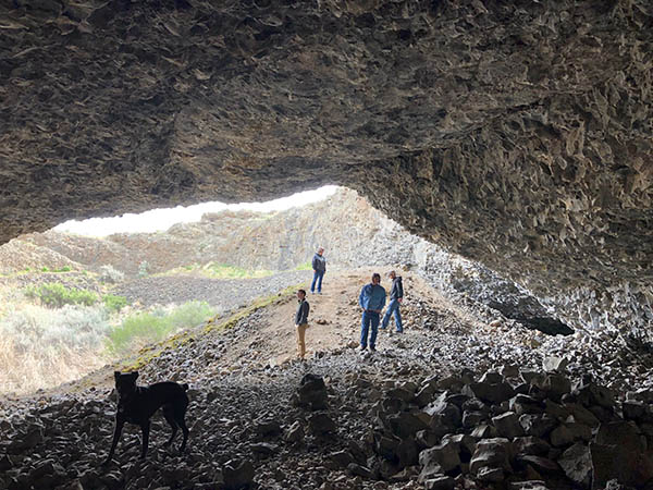 Photo of four people and a dog standing inside a cave entrance.