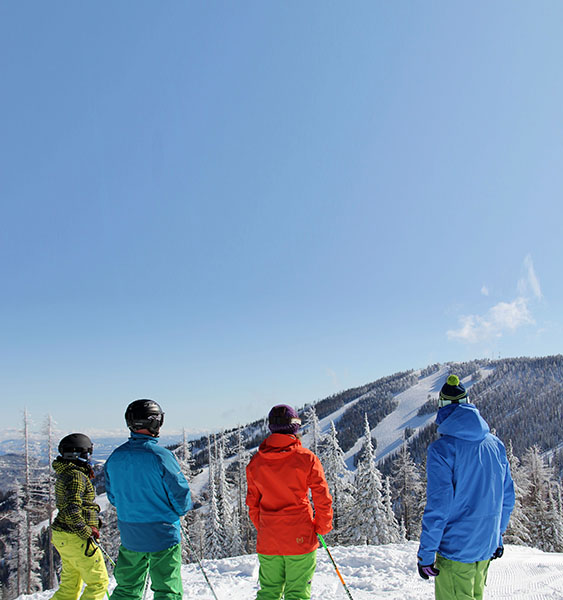 Photo of four skiers wearing brightly colored ski jackets taken from behind.