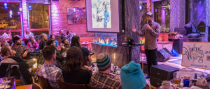 Photo of announcer addressing a crowd inside a bar.