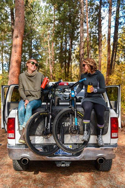 Photo of two girls and their bikes sitting on the back of pickup truck with the tailgate down.