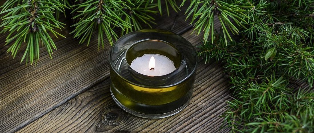 Photo of small candle in glass votive and evergreen branch.