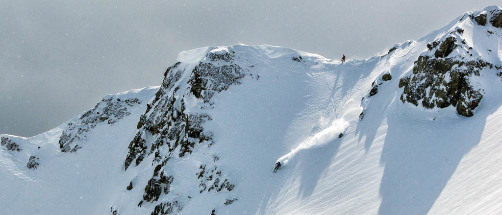 photo of backcountry skier on mountain peak from a distance.
