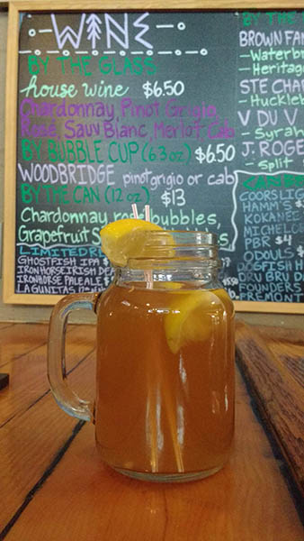 Photo of Hot Toddy served in a mason jar in front of menu board.