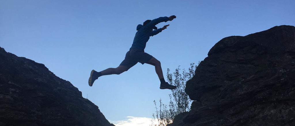 Silhouette of man leaping from one boulder to the next.