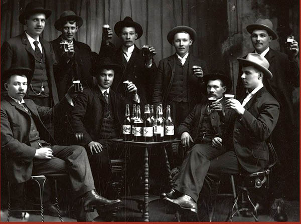 Historic photo of men sitting around a table with bottles of alcohol.