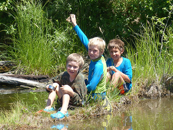 Photo of three boys sitting on a river bank.