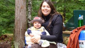 Mom sitting at a picnic table bench holding her baby on her lap.